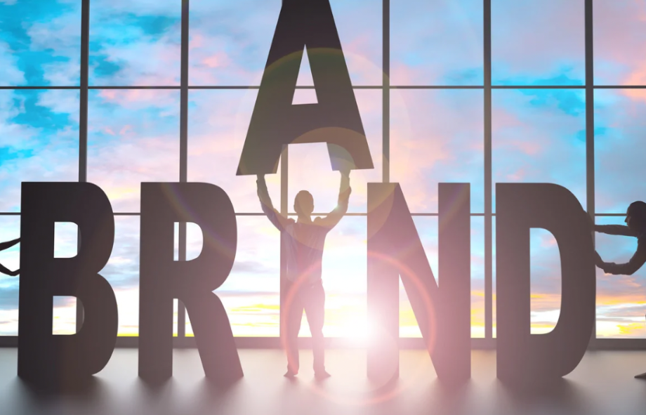 Silhouettes of people assembling large letters spelling “BRAND” in front of a window, symbolizing building a digital brand system.