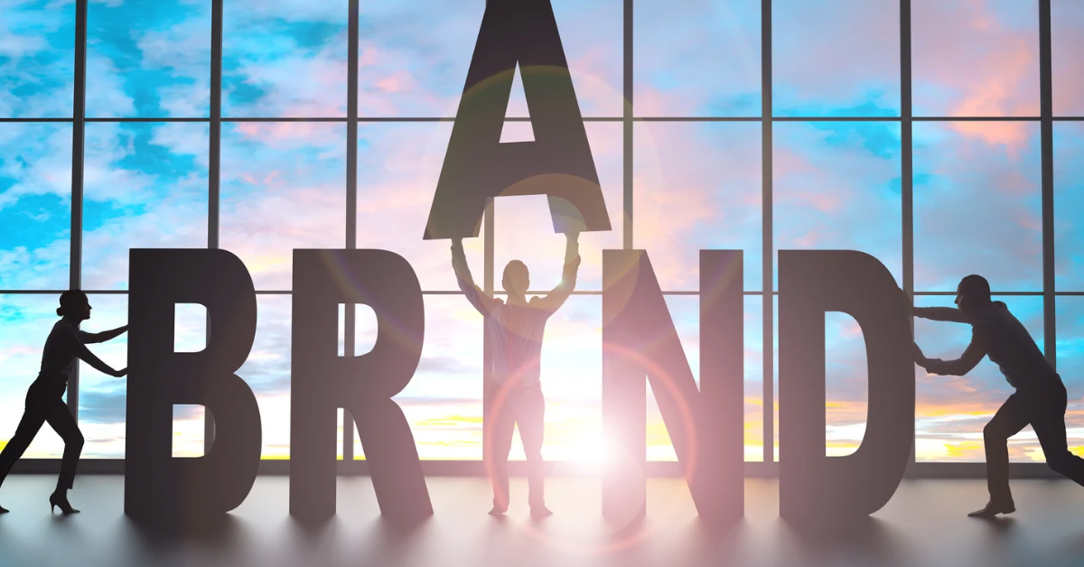 Silhouettes of people assembling large letters spelling “BRAND” in front of a window, symbolizing building a digital brand system.