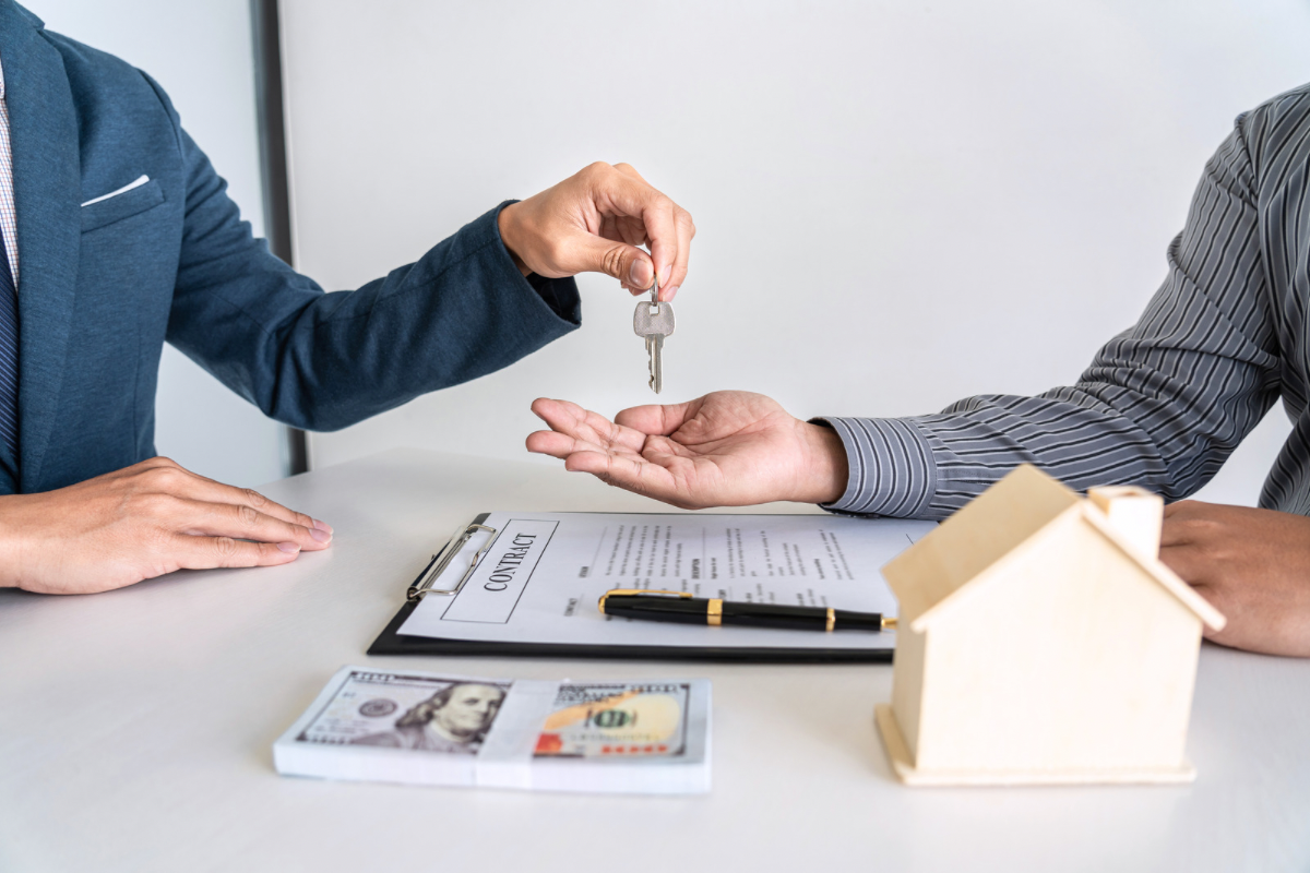 A salesperson handing keys to a customer over a signed contract, symbolizing the moment hesitation is removed and a high-stakes decision is made.
