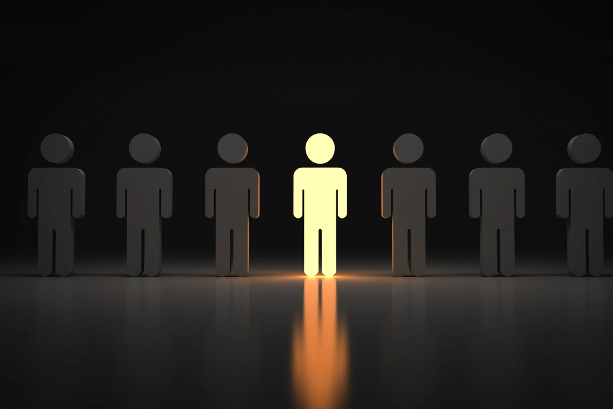 A single glowing yellow human figure standing out among a row of gray figures, symbolizing how strategic positioning makes a brand meaningfully different.