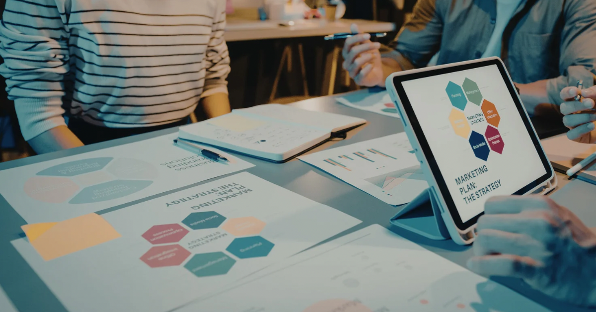 A team of professionals sitting around a table reviewing a digital marketing strategy diagram on a tablet screen during a meeting.