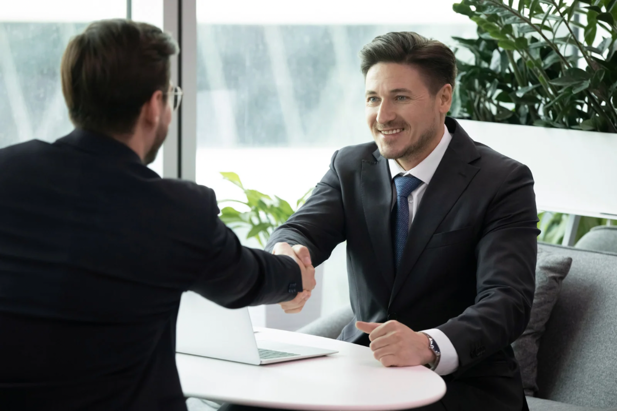 Two businessmen smiling and shaking hands across a desk, representing successful brand positioning and business growth.