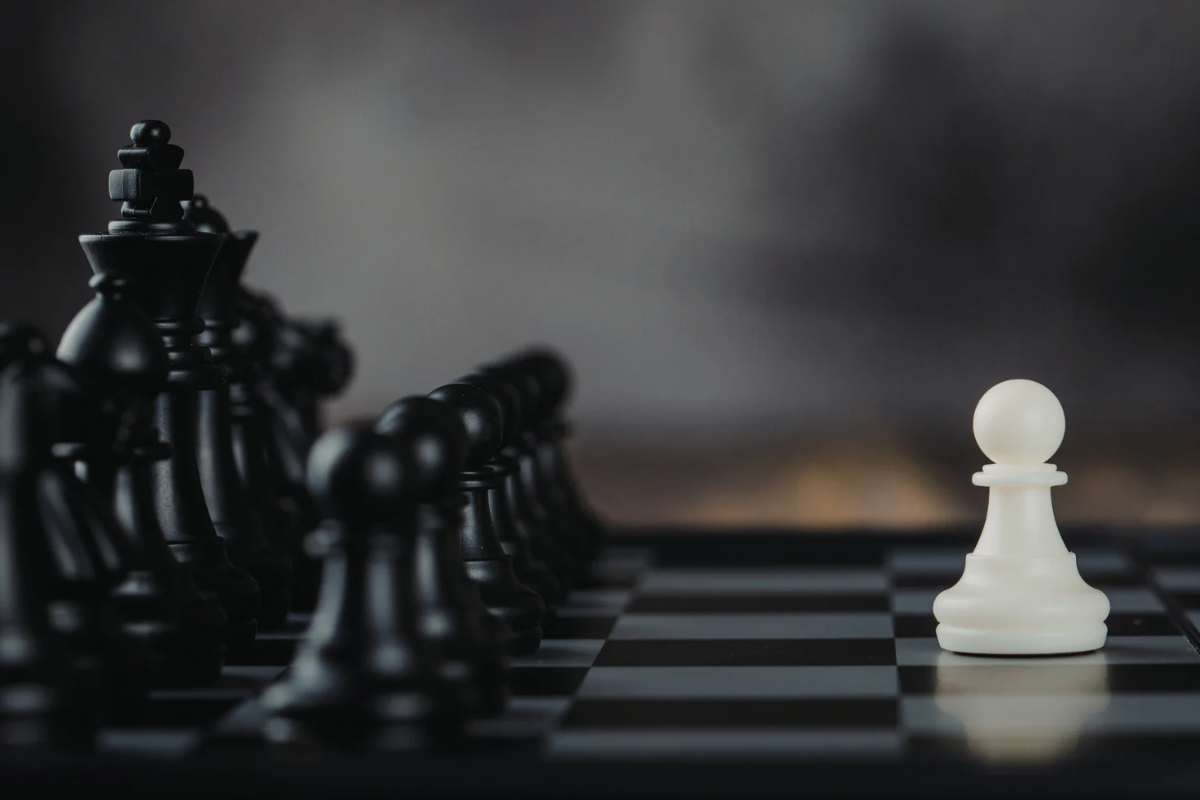 A single white chess piece facing a row of black chess pieces on a chessboard.