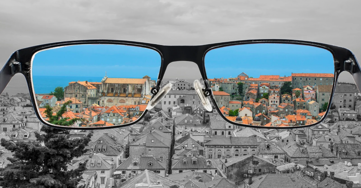 A pair of eyeglasses framing a cityscape in color against a mostly black-and-white background.