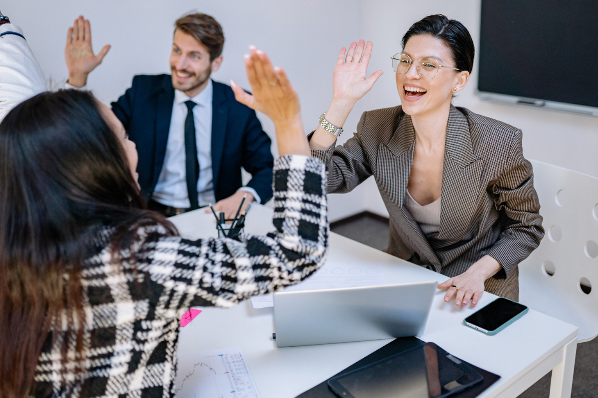 Coworkers in a meeting room smiling and high-fiving across a desk.