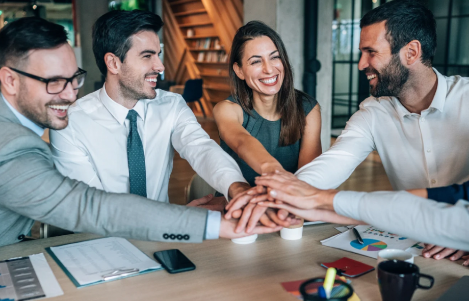 A team of employees smiling and placing their hands together during a meeting.
