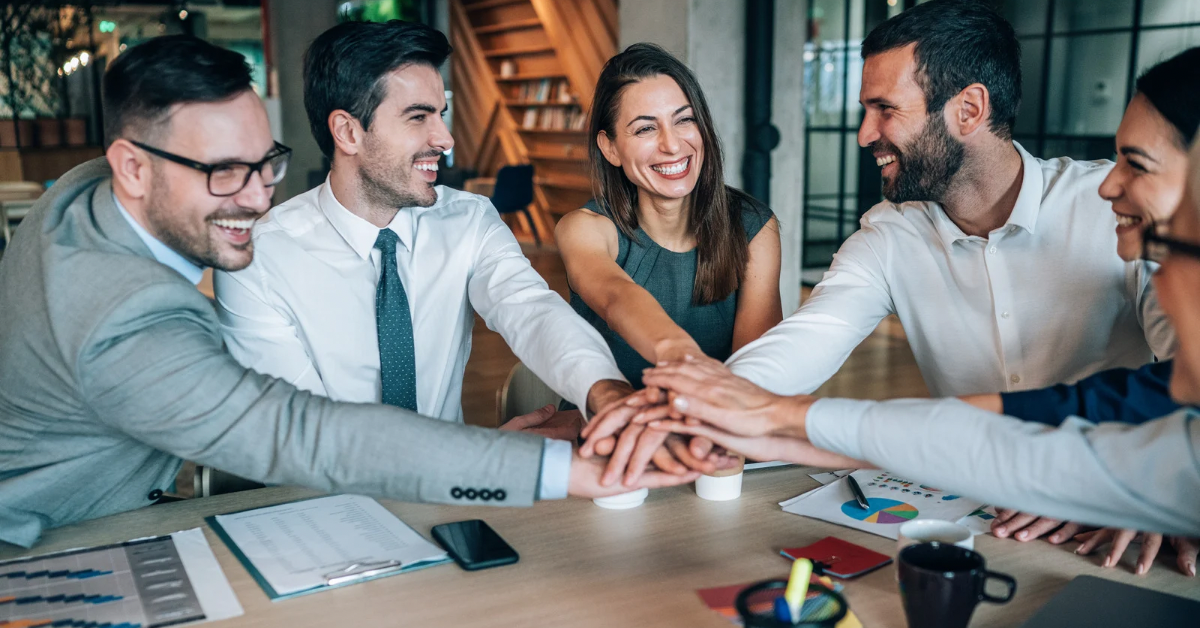 A team of employees smiling and placing their hands together during a meeting.