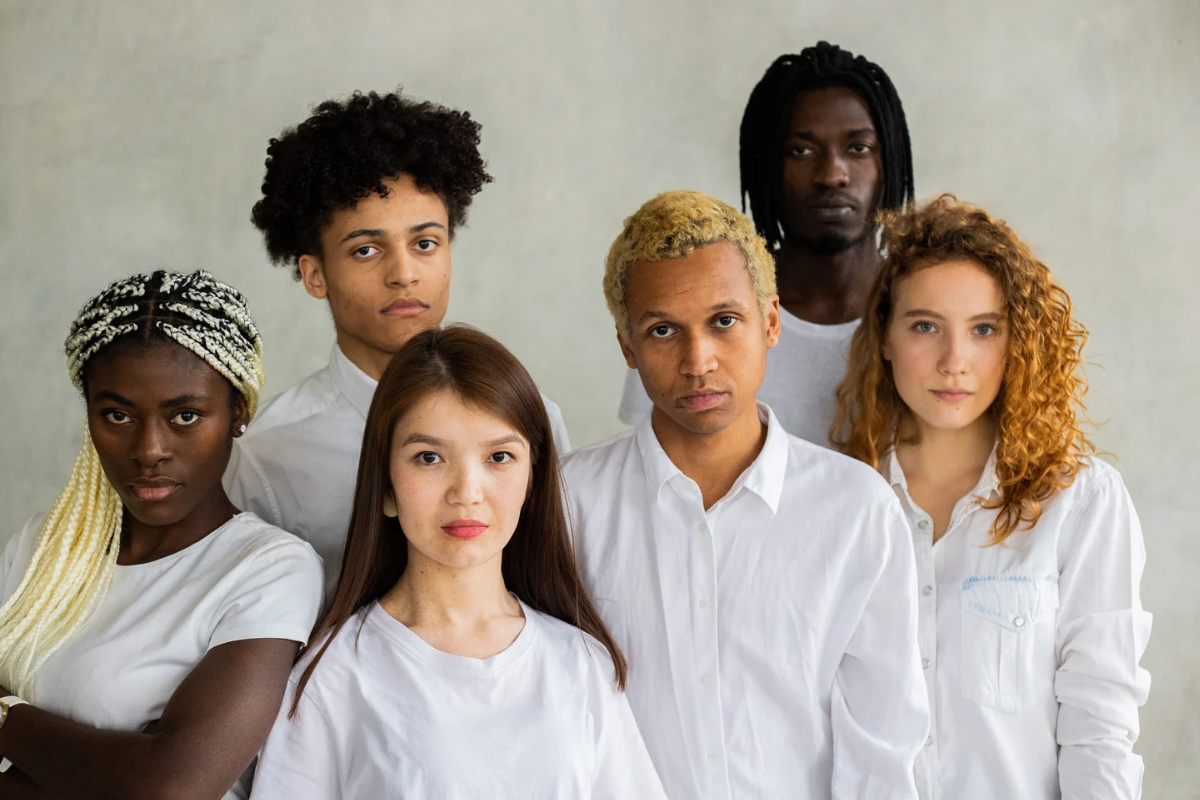A diverse group of six young adults standing closely together, all wearing white shirts and looking at the camera.