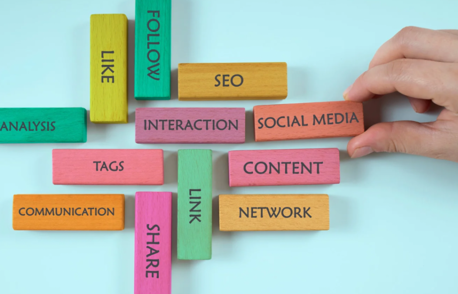 A hand arranging colorful wooden blocks labeled social media, SEO, content, communication, and interaction on a blue background.