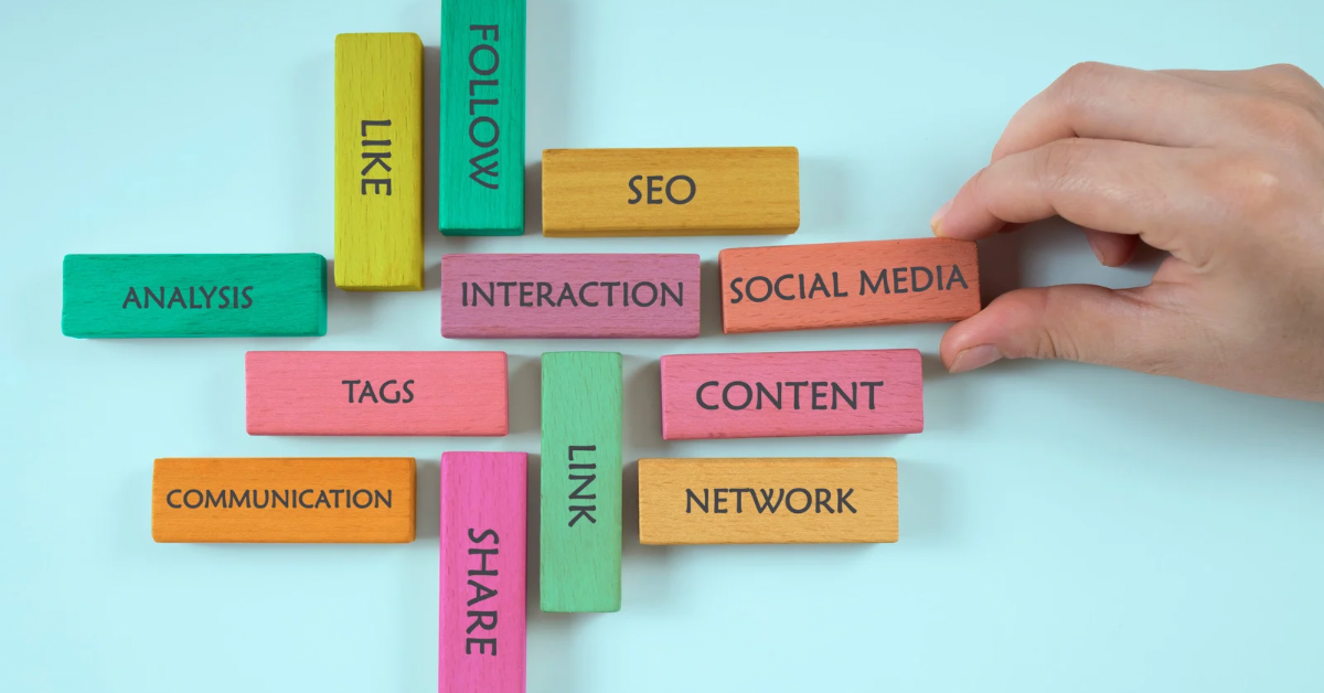 A hand arranging colorful wooden blocks labeled social media, SEO, content, communication, and interaction on a blue background.