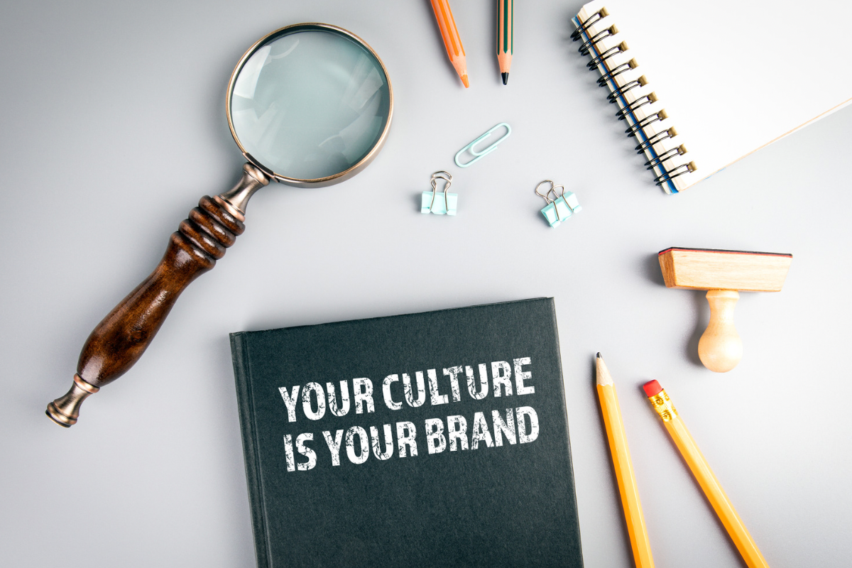 A notebook printed with the words “Your culture is your brand” surrounded by office tools on a desk.
