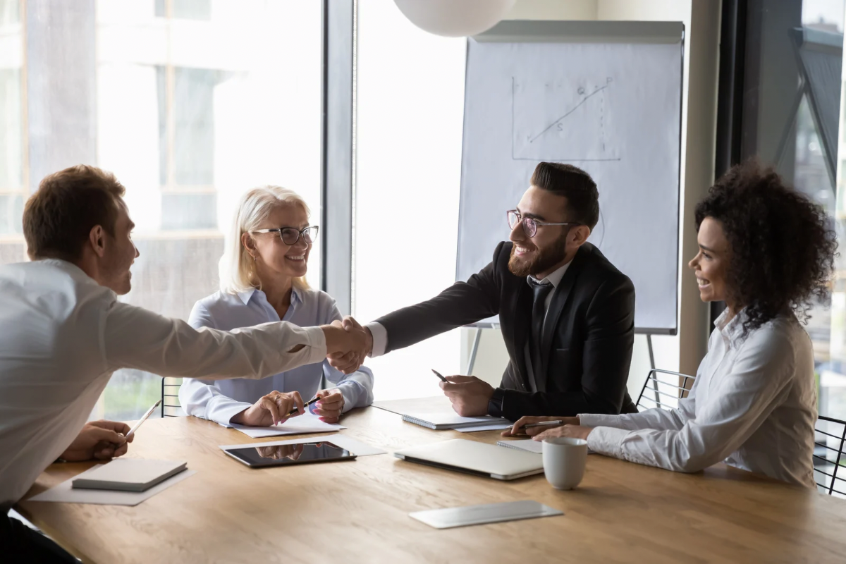 Two professionals shaking hands across a meeting table symbolizing successful brand facilitation and mutual trust