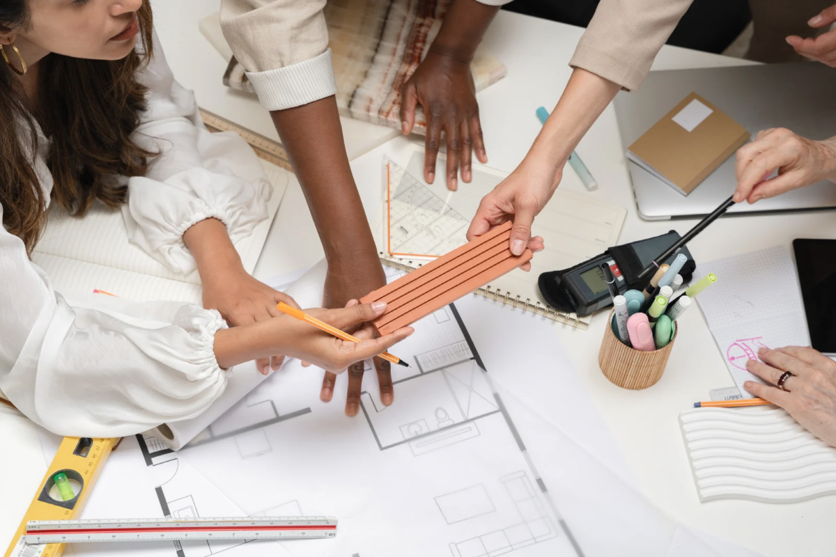 Multiple hands working together over architectural blueprints to build a cohesive strategic narrative.