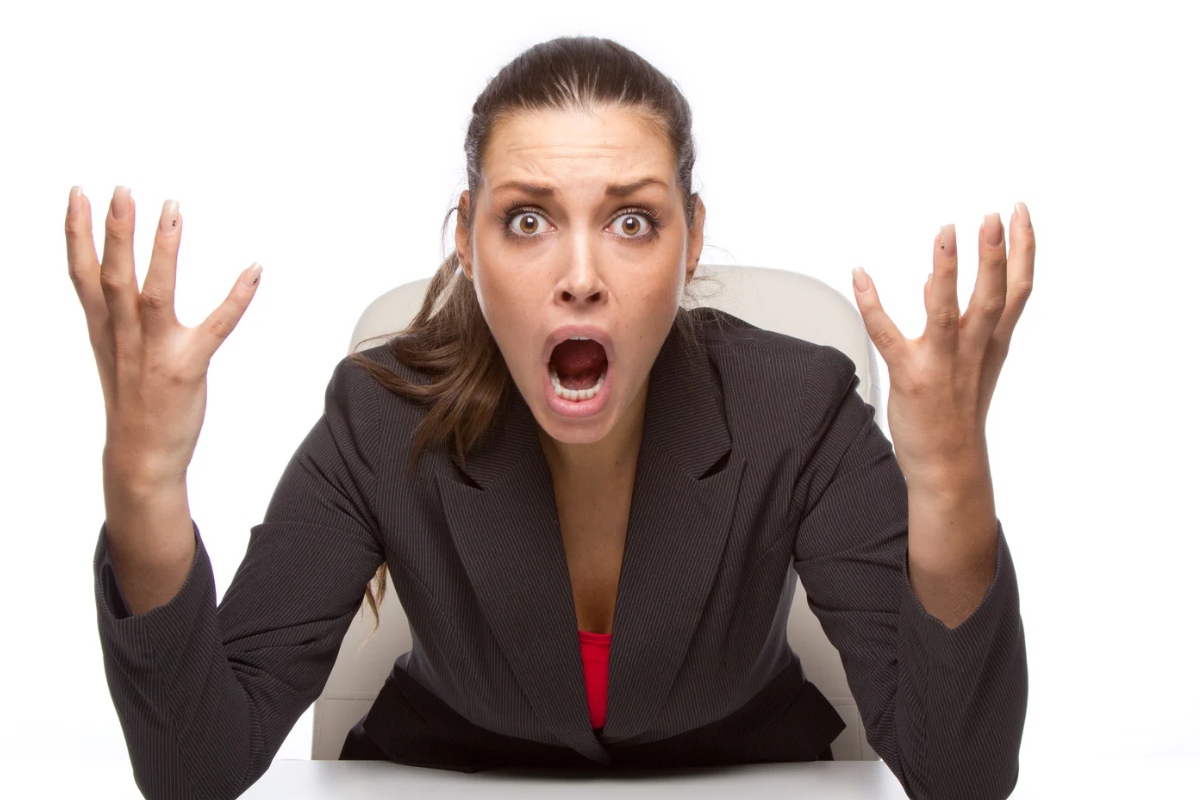 A businesswoman looking highly stressed and overwhelmed with her hands raised in exasperation.